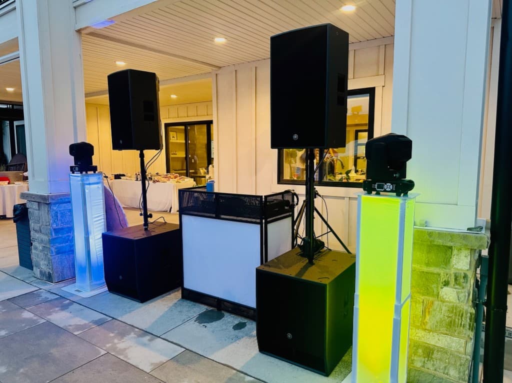 Outdoor speakers, subs, and lighting towers set up on a patio for a reception